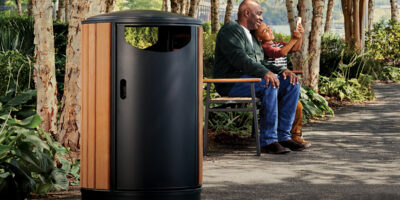 Grandfather and grandson sitting on a bench taking selfies together with wood and metal litter receptacle in foreground