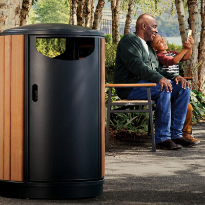 Grandfather and grandson sitting on a bench taking selfies together with wood and metal litter receptacle in foreground