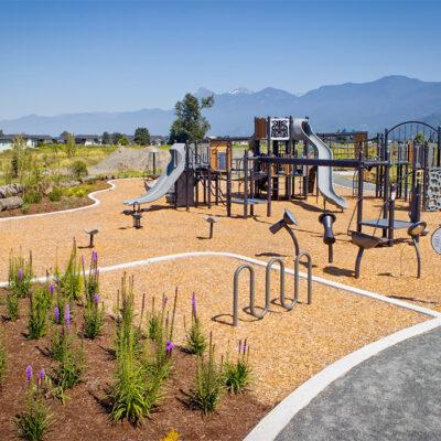 A silver playground on wood chip surfacing with purple flowers bordering it