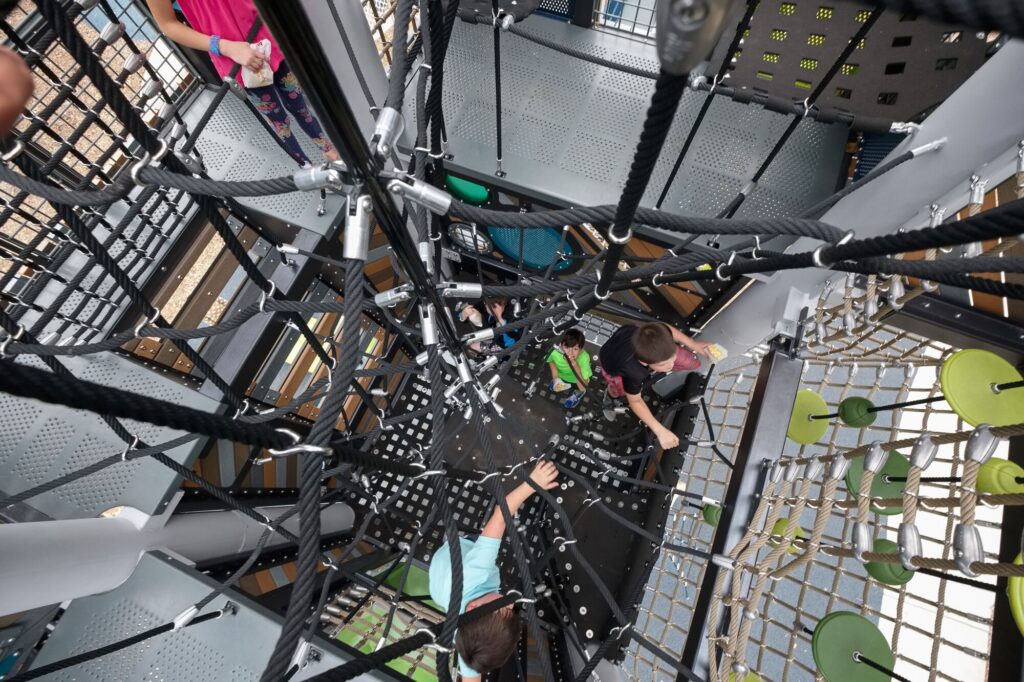 risky play showing kids climbing through a maze of nets inside a playground tower