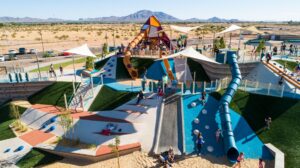 big playground on the side of a hill with a long blue slide and a mountain shaped play tower on top