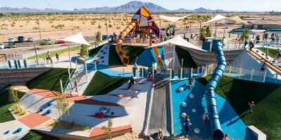 big playground on the side of a hill with a long blue slide and a mountain shaped play tower on top