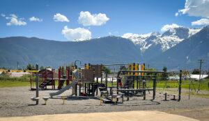 Grey and Yellow playground on gravel with mountains in background