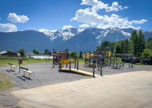 Grey and Yellow playground on gravel with mountains in background