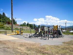 Grey and Yellow playground on gravel with totem pole in background