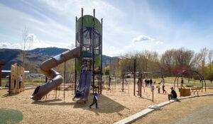 Green and brown playground tower with horizontal and vertical logs and swings on wood fibre surfacing