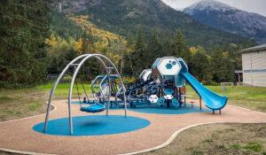 Futuristic blue, silver, and brown playground on PIP rubber surfacing with mountains and trees in the background