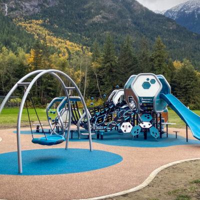 Futuristic blue, silver, and brown playground on PIP rubber surfacing with mountains and trees in the background