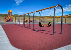 Red, yellow, and black playground and swings on PIP rubber surfacing