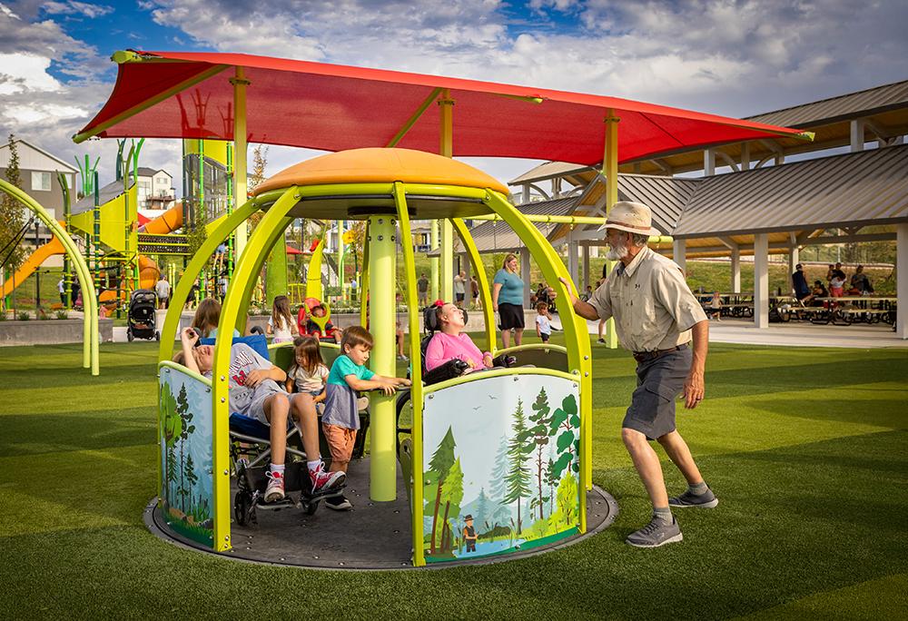 man pushing kids in a we-go-round on turf