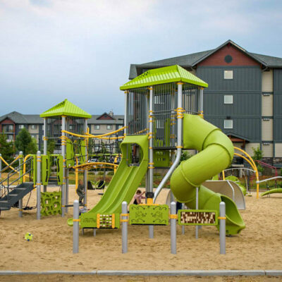 A playground with a slide and a building in the background.