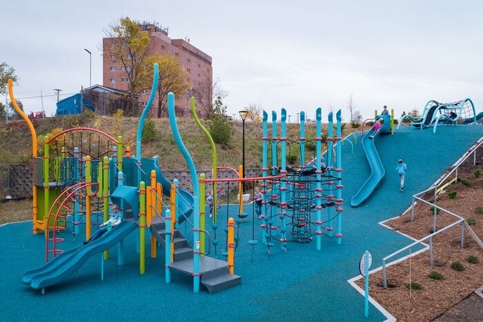 a playground at the bottom of a hill with a slide and net climber on the hill